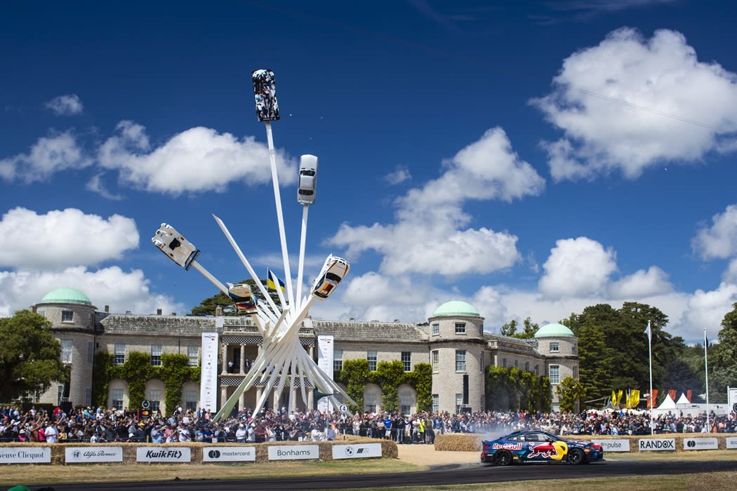 A huge outdoor sculpture, with cars at the tops of white beams seemingly flying upwards