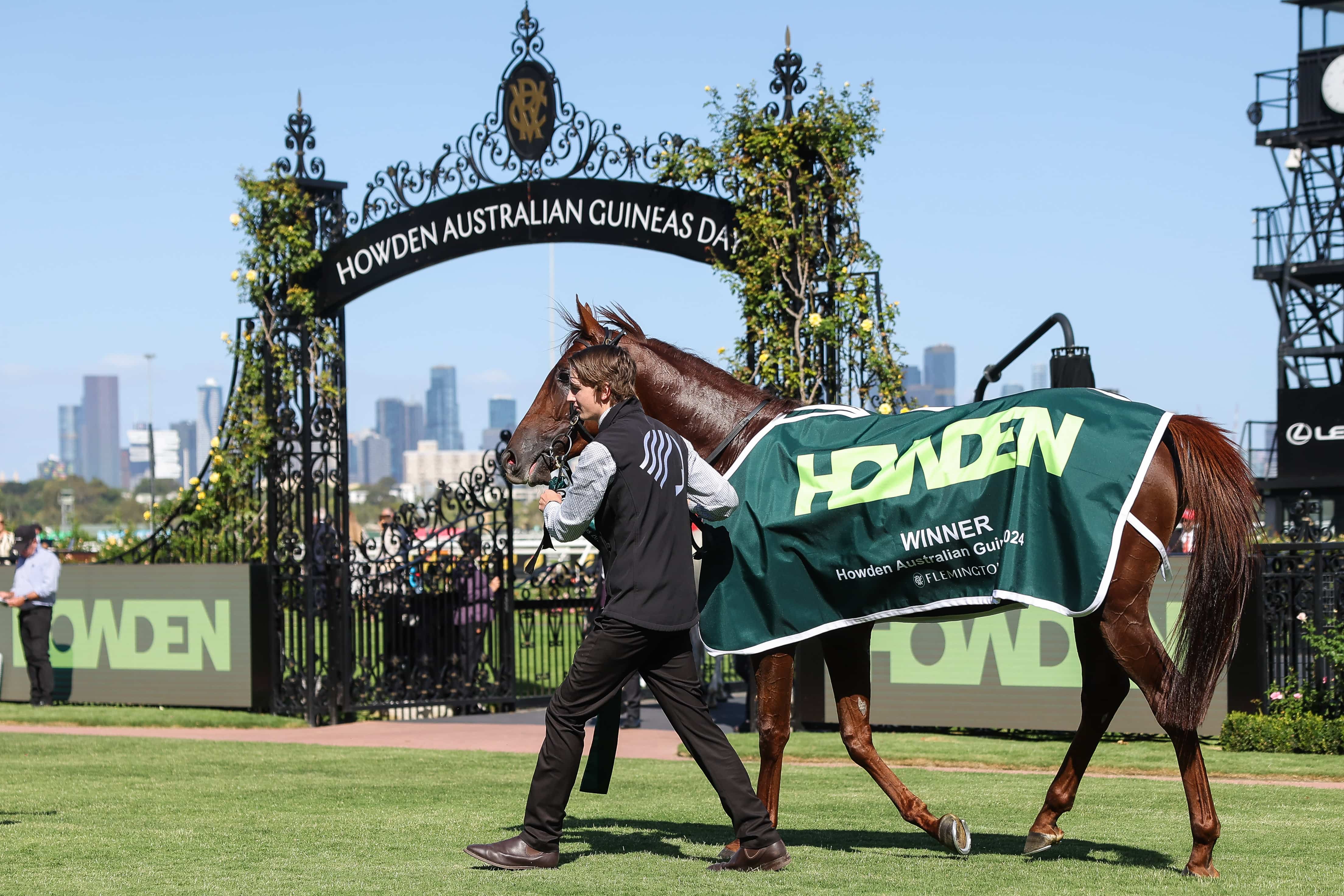 A horse wearing a Howden-branded winner's rug being led near the gate that reads Howden Australian Guineas Day