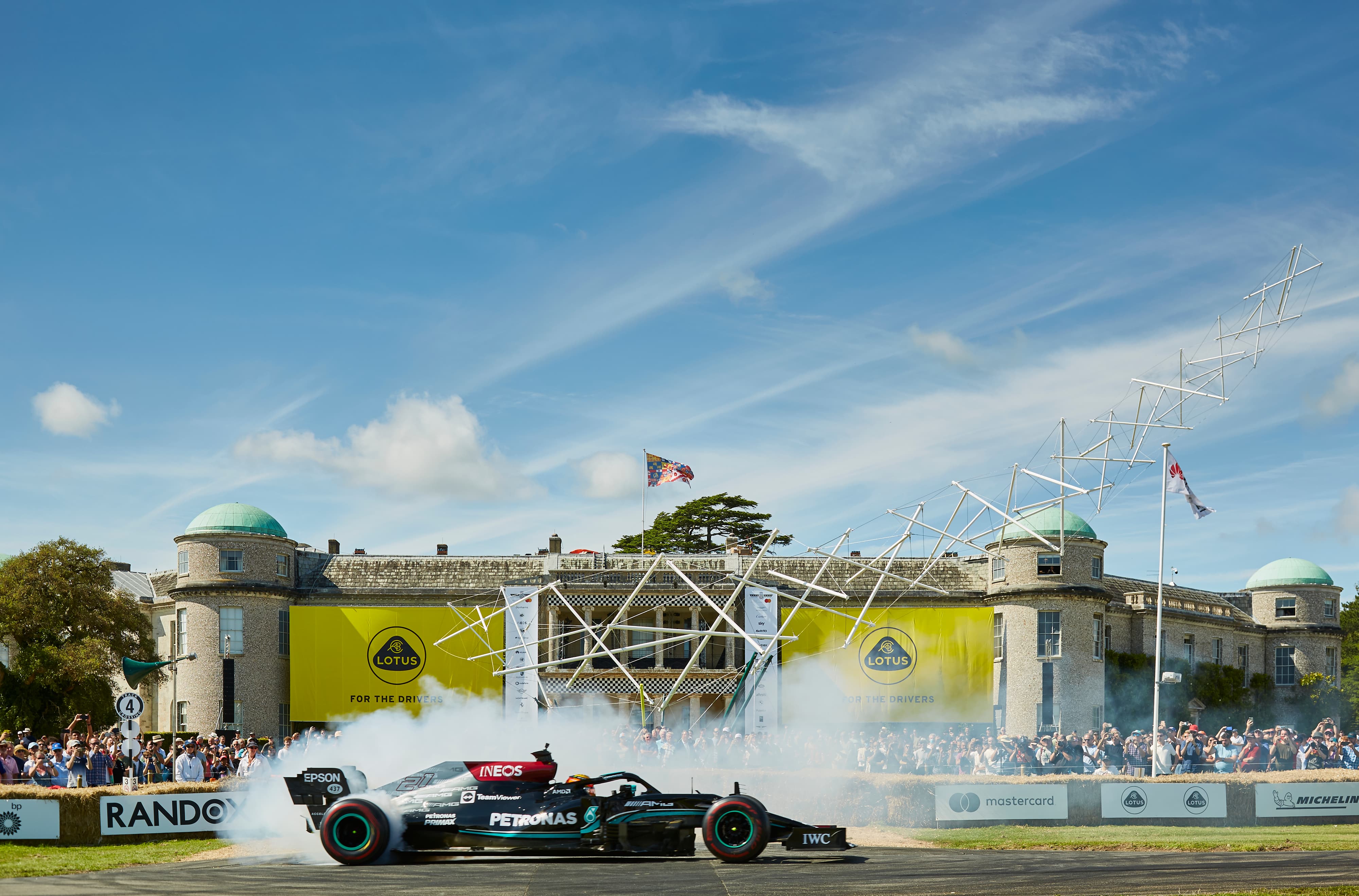 A crowd cheering on a race car on a sunny day at Goodwood